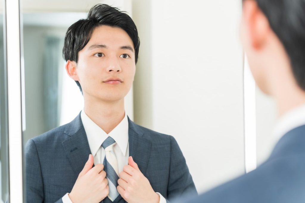 鏡を見て身だしなみを整える男性