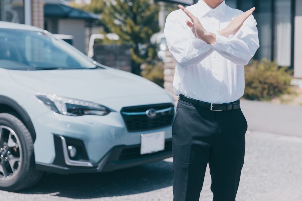 車の前でバツサインを出す男性